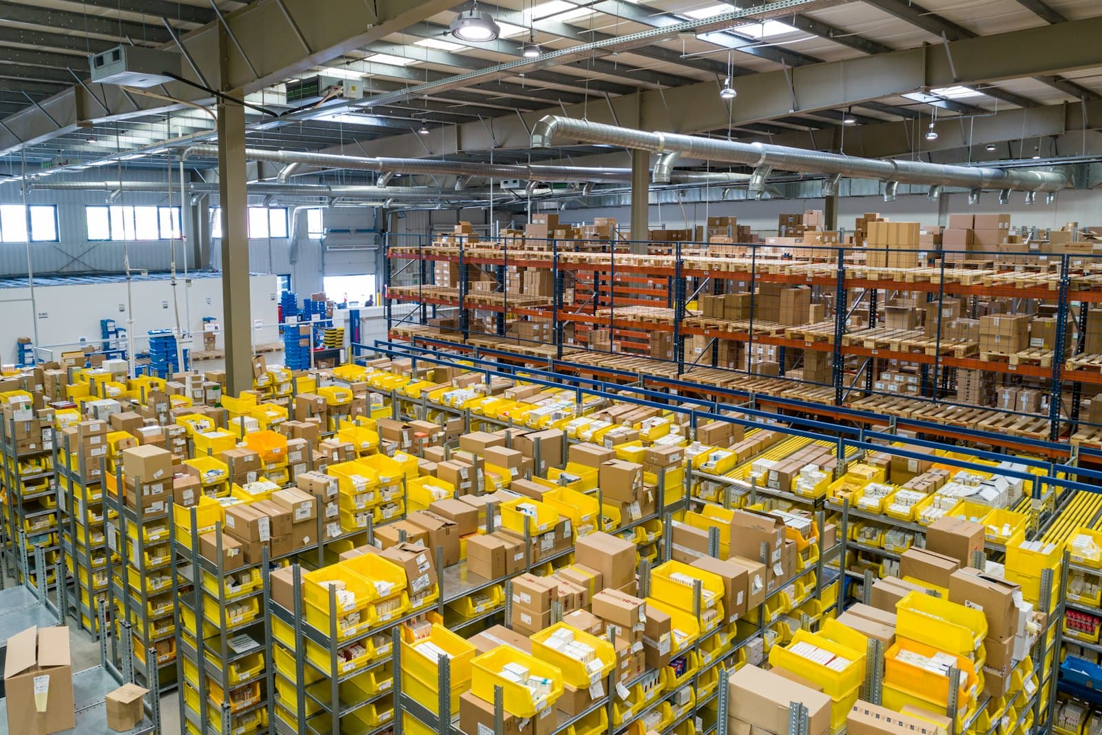 A forklift operator moving wrapped pallets inside a warehouse with yellow safety barriers.